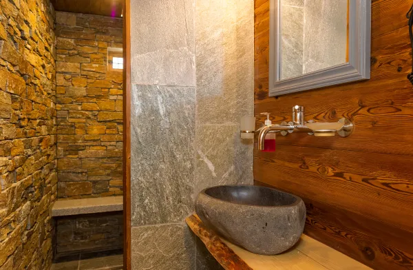 Salle de bains avec vasque en pierre, sous-vasque en bois, murs en pierre de la douche