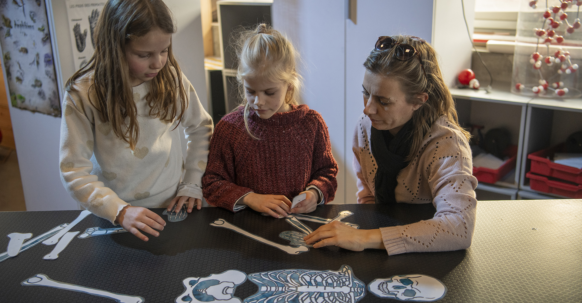 Une mère avec ses filles devant un squelette en papier