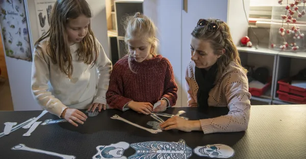 Une mère avec ses filles devant un squelette en papier